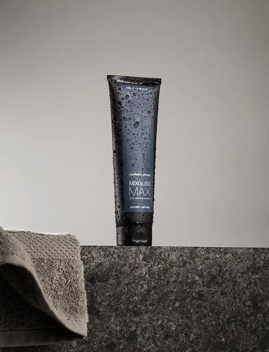 Tube of Mixgliss Max lubricant on a gray surface with a towel in the background