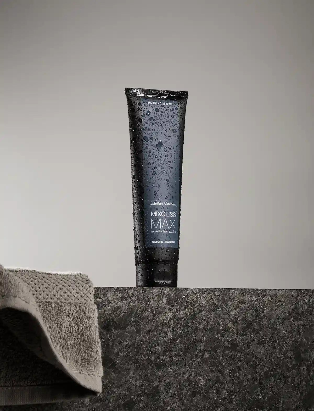 Tube of Mixgliss Max lubricant on a gray surface with a towel in the background