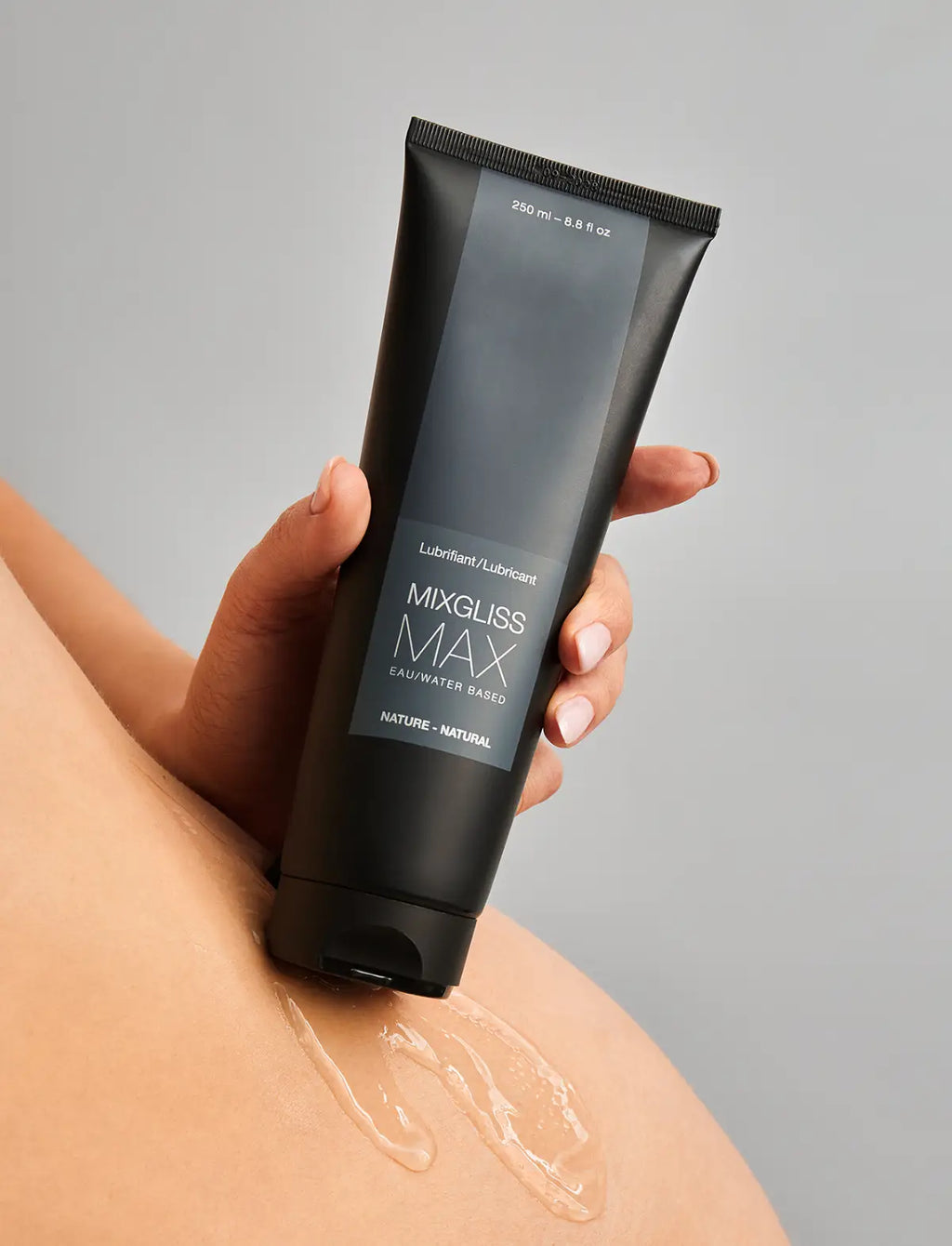 Hand holding a tube of Mixgliss Max lubricant on a gray background